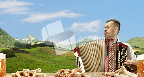 Image of The happy smiling man with beer dressed in traditional Austrian or Bavarian costume holding mug of beer, mountains on background, flyer