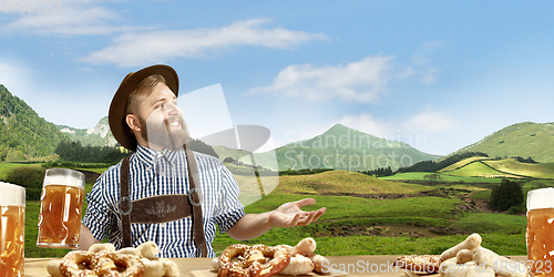 Image of The happy smiling man with beer dressed in traditional Austrian or Bavarian costume holding mug of beer, mountains on background, flyer