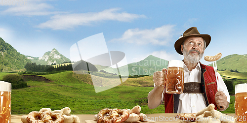 Image of The senior happy smiling man with beer dressed in traditional Austrian or Bavarian costume holding mug of beer, mountains on background, flyer