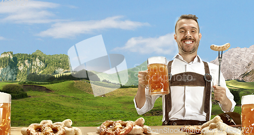 Image of The happy smiling man with beer dressed in traditional Austrian or Bavarian costume holding mug of beer, mountains on background, flyer