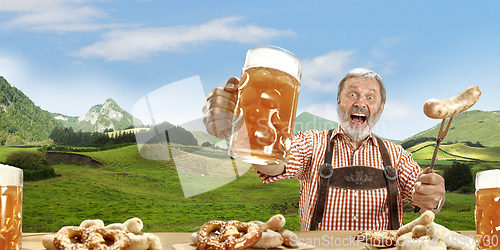 Image of The senior happy smiling man with beer dressed in traditional Austrian or Bavarian costume holding mug of beer, mountains on background, flyer