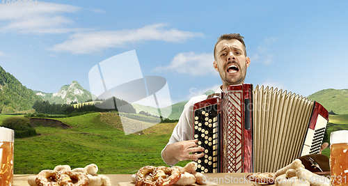 Image of The happy smiling man with beer dressed in traditional Austrian or Bavarian costume holding mug of beer, mountains on background, flyer