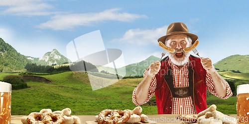 Image of The senior happy smiling man with beer dressed in traditional Austrian or Bavarian costume holding mug of beer, mountains on background, flyer