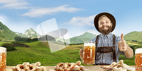 Image of The happy smiling man with beer dressed in traditional Austrian or Bavarian costume holding mug of beer, mountains on background, flyer