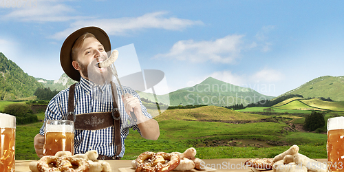 Image of The happy smiling man with beer dressed in traditional Austrian or Bavarian costume holding mug of beer, mountains on background, flyer