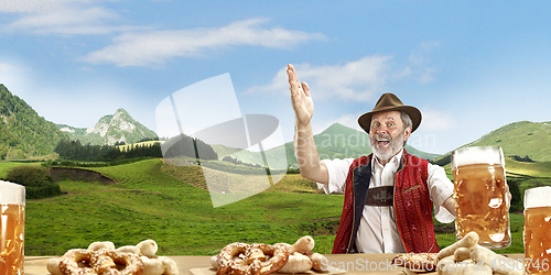 Image of The senior happy smiling man with beer dressed in traditional Austrian or Bavarian costume holding mug of beer, mountains on background, flyer