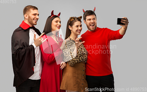 Image of happy friends in halloween costumes taking selfie