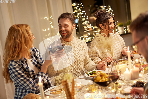 Image of happy friends drinking red wine at christmas party