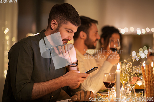 Image of man with smartphone at dinner party with friends