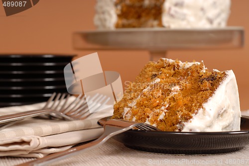 Image of Carrot cake with forks, plates, and whole cake in background