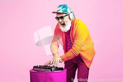 Image of Senior hipster man wearing eyeglasses posing on pink background. Tech and joyful elderly lifestyle concept