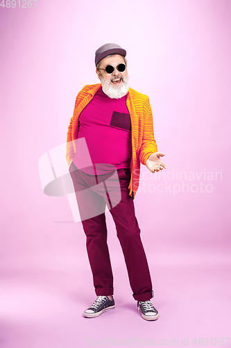 Image of Senior hipster man wearing eyeglasses posing on pink background. Tech and joyful elderly lifestyle concept