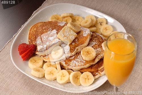 Image of Banana pancakes with maple syrup, a strawberrry and orange juice