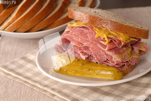 Image of Corned beef sandwich with mustard and pickle on rye