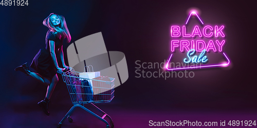 Image of Portrait of young woman in neon light on dark backgound. The human emotions, black friday, cyber monday, purchases, sales, finance concept. Neoned lettering.