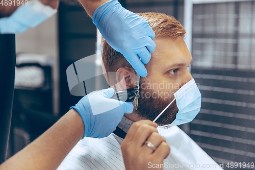 Image of Man getting hair cut at the barbershop wearing mask during coronavirus pandemic