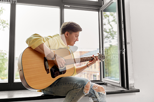 Image of young man playing guitar sitting on windowsill