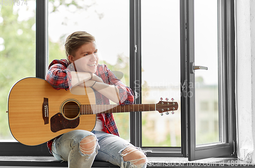 Image of young man playing guitar sitting on windowsill