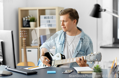 Image of young man with computer playing guitar at home