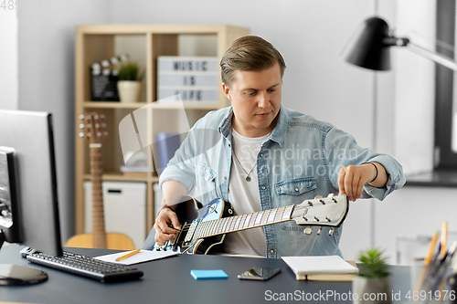 Image of young man with computer playing guitar at home