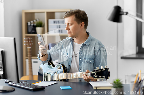 Image of young man with smartphone and guitar at home