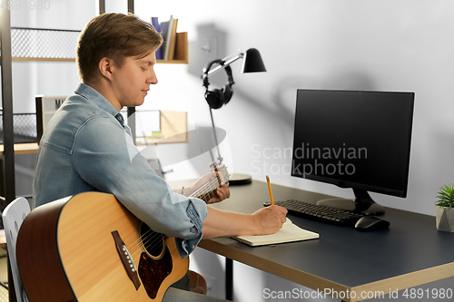 Image of man with guitar writing to music book at home