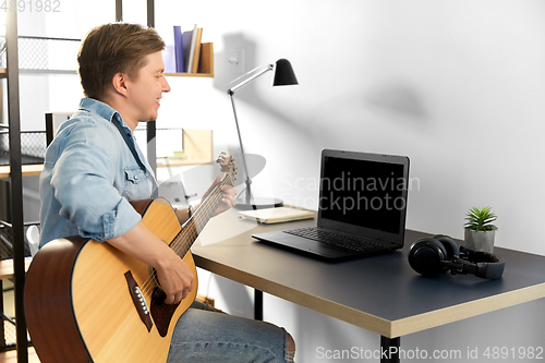 Image of young man with laptop and guitar at home