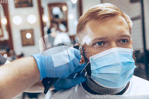 Image of Man getting hair cut at the barbershop wearing mask during coronavirus pandemic