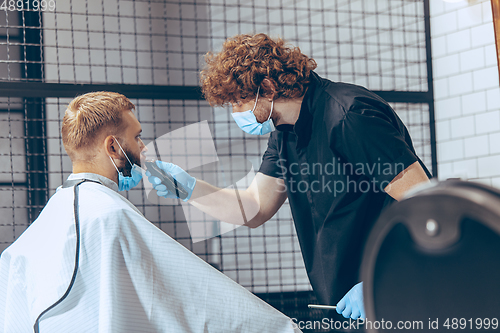 Image of Man getting hair cut at the barbershop wearing mask during coronavirus pandemic