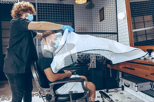 Image of Man getting hair cut at the barbershop wearing mask during coron