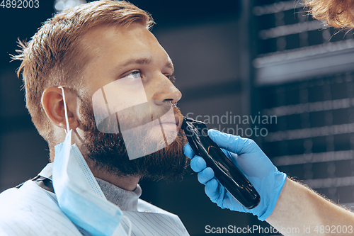 Image of Man getting hair cut at the barbershop wearing mask during coronavirus pandemic