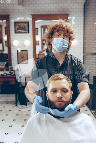 Image of Man getting hair cut at the barbershop wearing mask during coronavirus pandemic