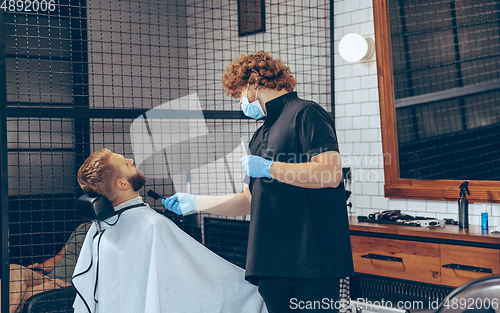 Image of Man getting hair cut at the barbershop wearing mask during coronavirus pandemic