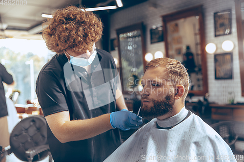 Image of Man getting hair cut at the barbershop wearing mask during coronavirus pandemic