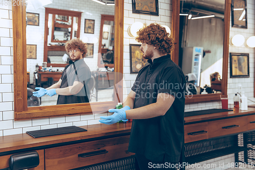 Image of Male barber at the barbershop wearing gloves preparing working place for client