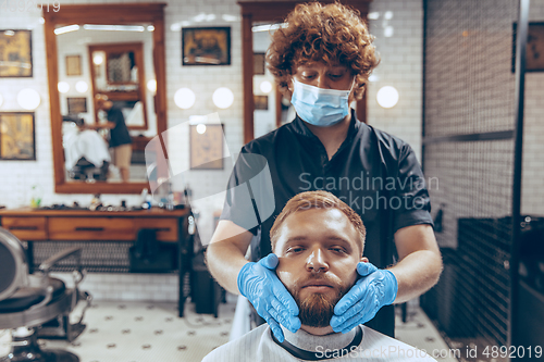 Image of Man getting hair cut at the barbershop wearing mask during coronavirus pandemic