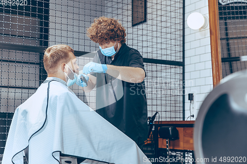 Image of Man getting hair cut at the barbershop wearing mask during coronavirus pandemic