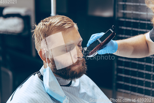 Image of Man getting hair cut at the barbershop wearing mask during coronavirus pandemic