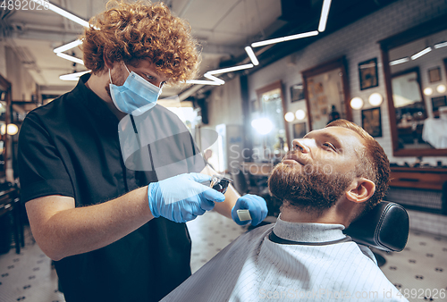 Image of Man getting hair cut at the barbershop wearing mask during coronavirus pandemic