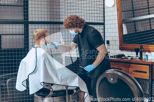 Image of Man getting hair cut at the barbershop wearing mask during coronavirus pandemic