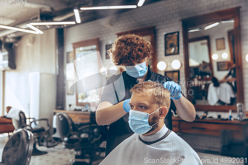 Image of Man getting hair cut at the barbershop wearing mask during coronavirus pandemic