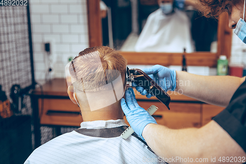 Image of Man getting hair cut at the barbershop wearing mask during coronavirus pandemic