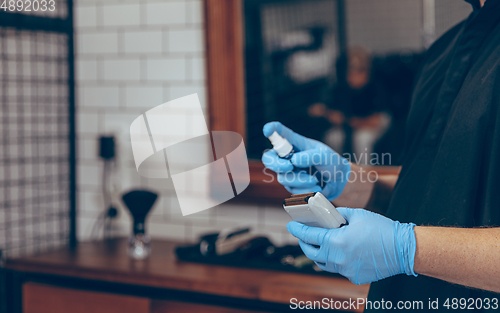 Image of Male barber at the barbershop wearing gloves preparing working place for client