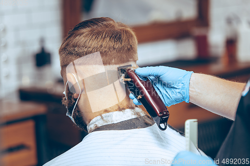 Image of Man getting hair cut at the barbershop wearing mask during coronavirus pandemic