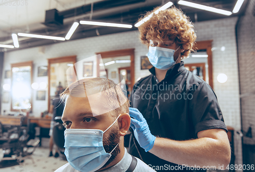 Image of Man getting hair cut at the barbershop wearing mask during coronavirus pandemic