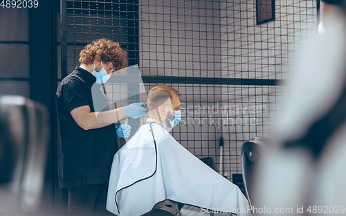 Image of Man getting hair cut at the barbershop wearing mask during coronavirus pandemic