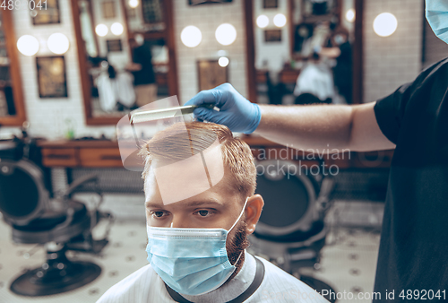 Image of Man getting hair cut at the barbershop wearing mask during coronavirus pandemic