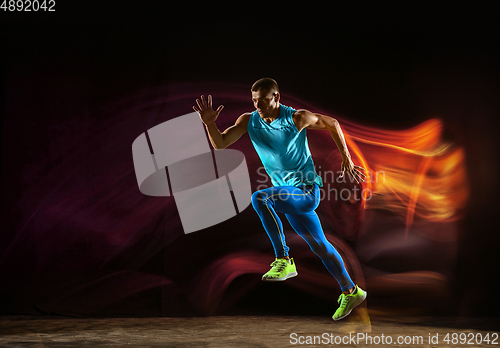 Image of Professional male runner training isolated on black studio background in mixed light