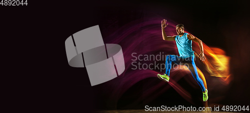 Image of Professional male runner training isolated on black studio background in mixed light