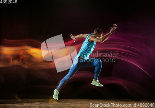 Image of Professional male runner training isolated on black studio background in mixed light